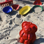 Gluckskafer plastic-free metal teddy bear shaped sand mould toy placed in the sand on a beach.