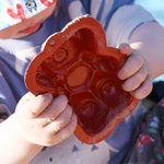 A close up of a red bear shaped sand mould in a child's hand. 