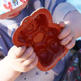 A close up of a red bear shaped sand mould in a child's hand. 