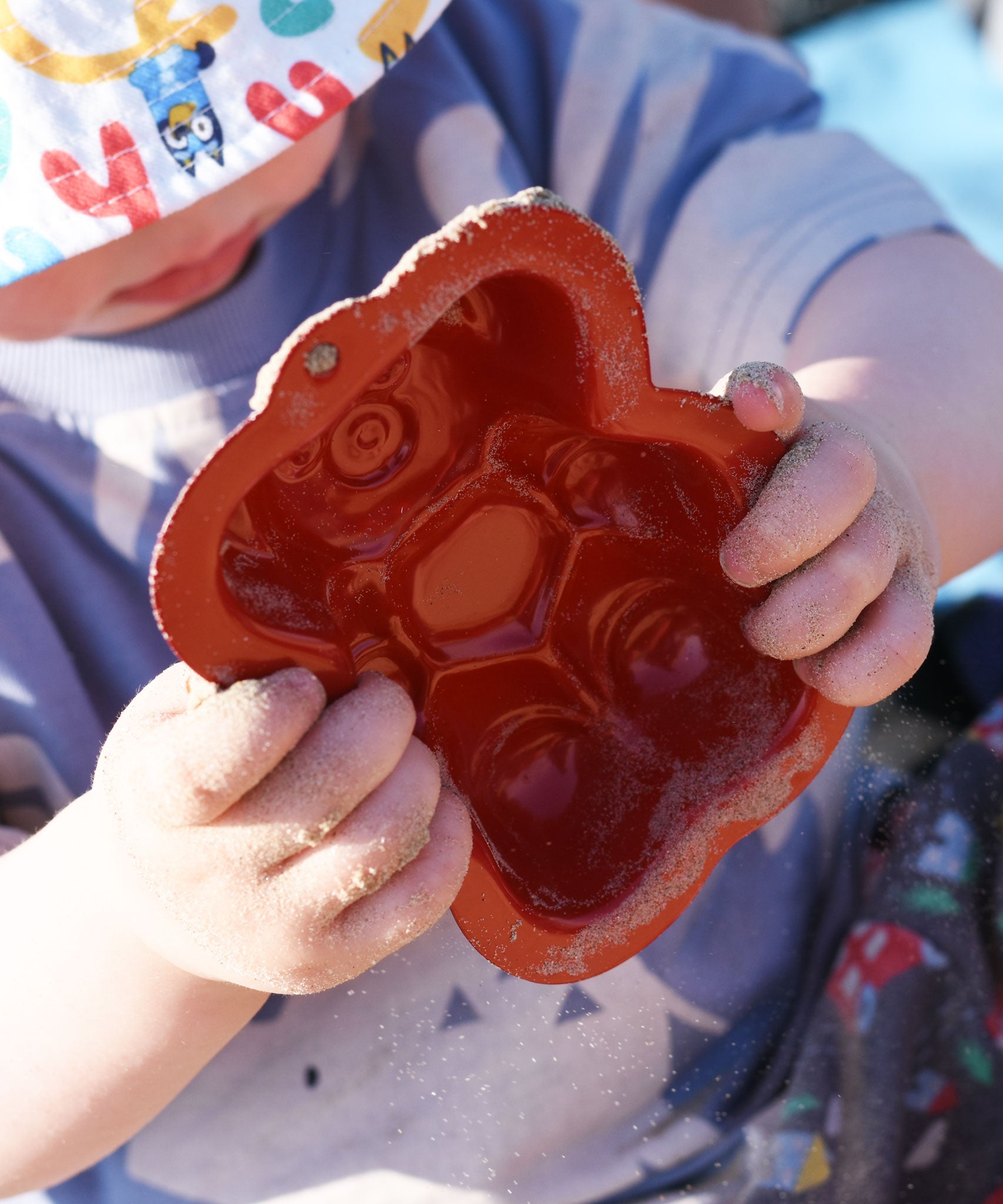 A close up of a red bear shaped sand mould in a child's hand. 