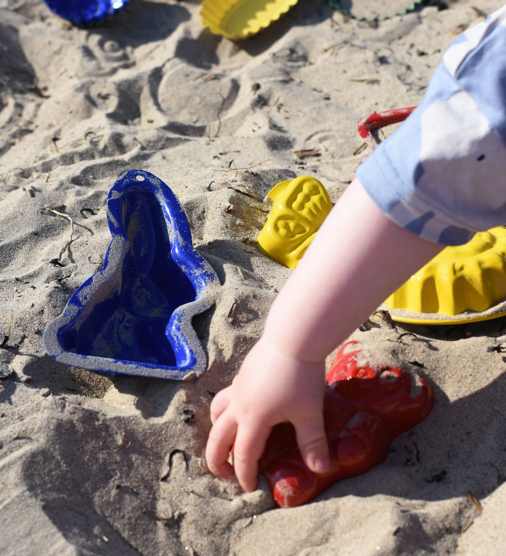 A child's hand playing with some Glückskäfer Metal Sand Moulds.