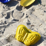 A Glückskäfer Metal butterfly shaped yellow coloured, Sand Mould placed on the sand at a beach. 
