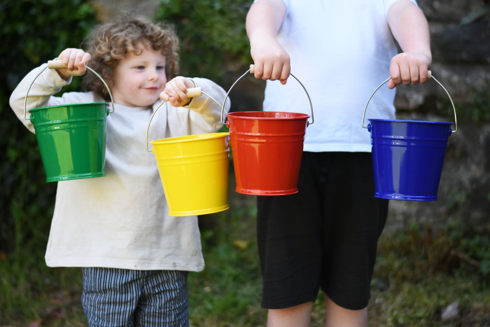 Four Glückskäfer Metal Buckets being held up in a line. There is a green, yellow, red and blue bucket. 