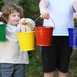 Four Glückskäfer Metal Buckets being held up in a line. There is a green, yellow, red and blue bucket. 