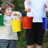 Four Glückskäfer Metal Buckets being held up in a line. There is a green, yellow, red and blue bucket. 