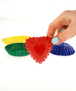 An adult's hand holding the red heart shaped fluted sand mould with the other moulds seen in the background.