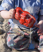 A child holding up a red teddy bear shaped sand mould.