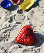 A Glückskäfer Metal red heart shaped Sand Mould placed on the sand at a beach. 