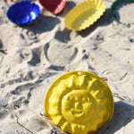 A Glückskäfer Metal Sun Sand Mould placed on the sand at a beach. Other sand moulds can be seen in the background. 
