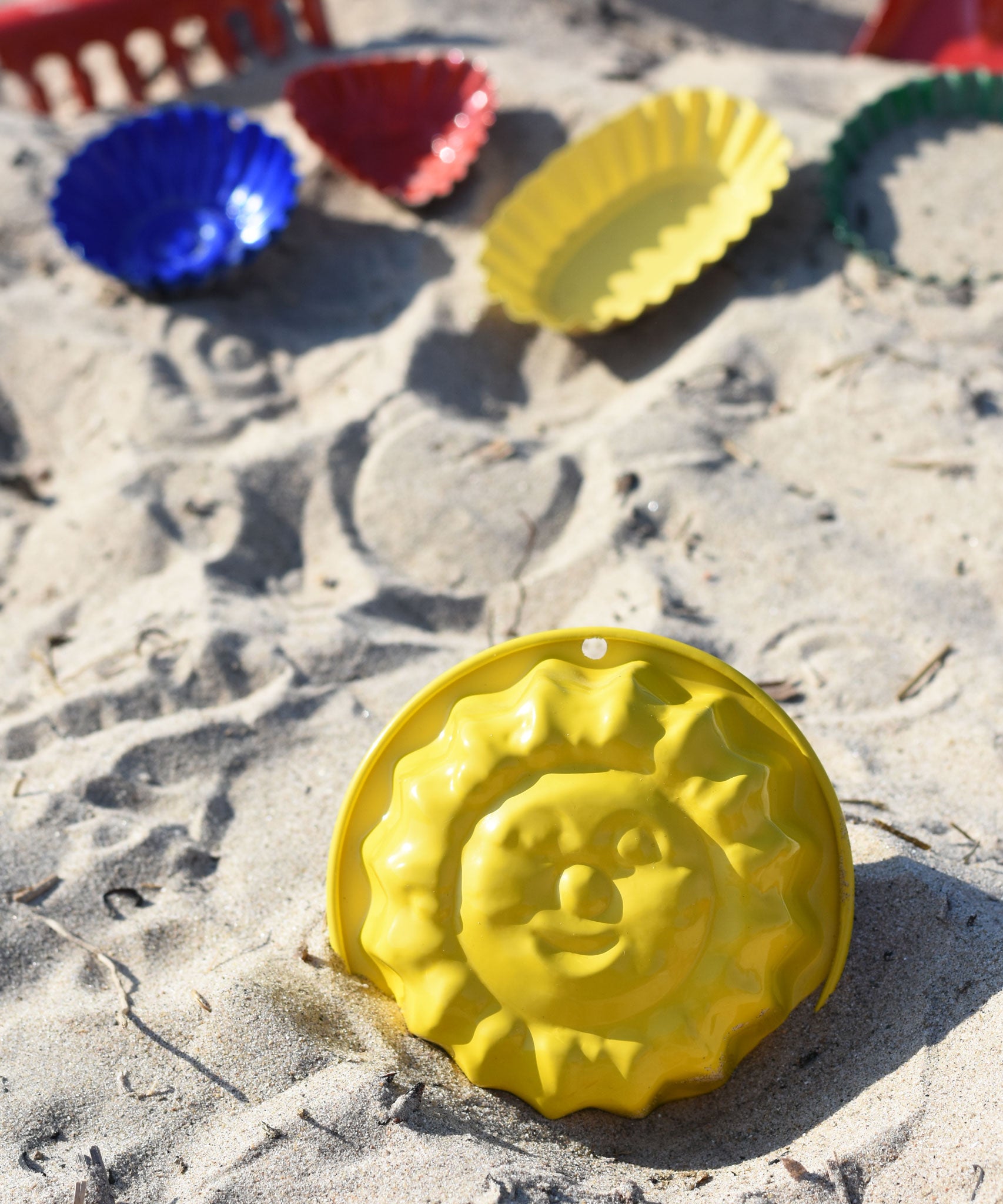 A Glückskäfer Metal Sun Sand Mould placed on the sand at a beach. Other sand moulds can be seen in the background. 