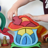A child's hand placing the mushroom shaped chimney piece onto the Glückskäfer Mushroom House wooden toy. 