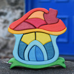 The Glückskäfer Mushroom House wooden stacking toy placed on a stone wall outdoors. 