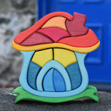 The Glückskäfer Mushroom House wooden stacking toy placed on a stone wall outdoors. 