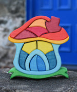 The Glückskäfer Mushroom House wooden stacking toy placed on a stone wall outdoors. 