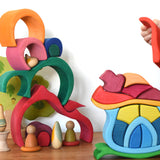 A child playing with the Glückskäfer Mushroom House wooden stacking toy. They have taken the red roof piece off the stack. The red gable house toy can be seen in the background  staked up to create a tower. 