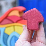A close up of the burgundy coloured mushroom shaped blocks from the Glückskäfer wooden Mushroom House Set in an adult's hand. 