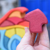 A close up of the burgundy coloured mushroom shaped blocks from the Glückskäfer wooden Mushroom House Set in an adult's hand. 