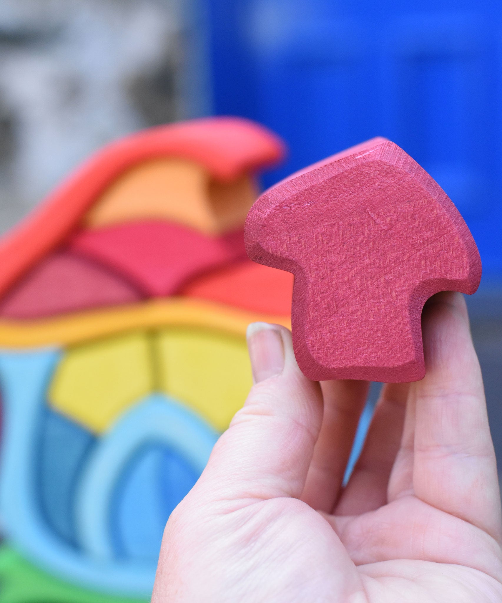 A close up of the burgundy coloured mushroom shaped blocks from the Glückskäfer wooden Mushroom House Set in an adult's hand. 