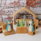 The The Gluckskafer Natural All-In House wooden toy shown with wooden peg dolls and Grapat mandala pieces. The peg dolls have been placed on the little seats and the the green cone shaped mandala pieces have been placed on the wooden table besides the. 
