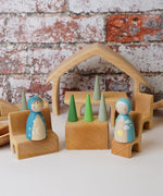 The The Gluckskafer Natural All-In House wooden toy shown with wooden peg dolls and Grapat mandala pieces. The peg dolls have been placed on the little seats and the the green cone shaped mandala pieces have been placed on the wooden table besides the. 