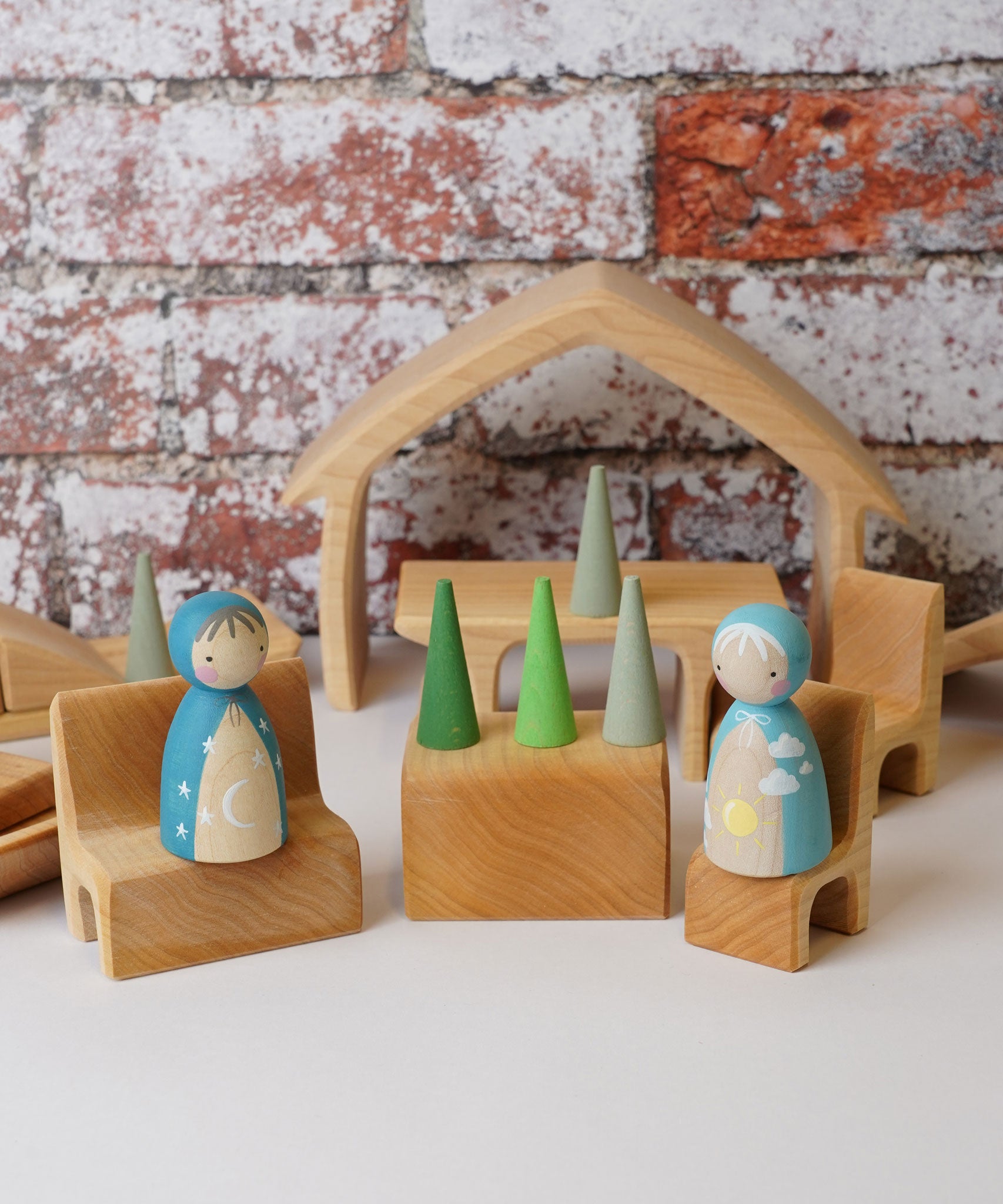 The The Gluckskafer Natural All-In House wooden toy shown with wooden peg dolls and Grapat mandala pieces. The peg dolls have been placed on the little seats and the the green cone shaped mandala pieces have been placed on the wooden table besides the. 