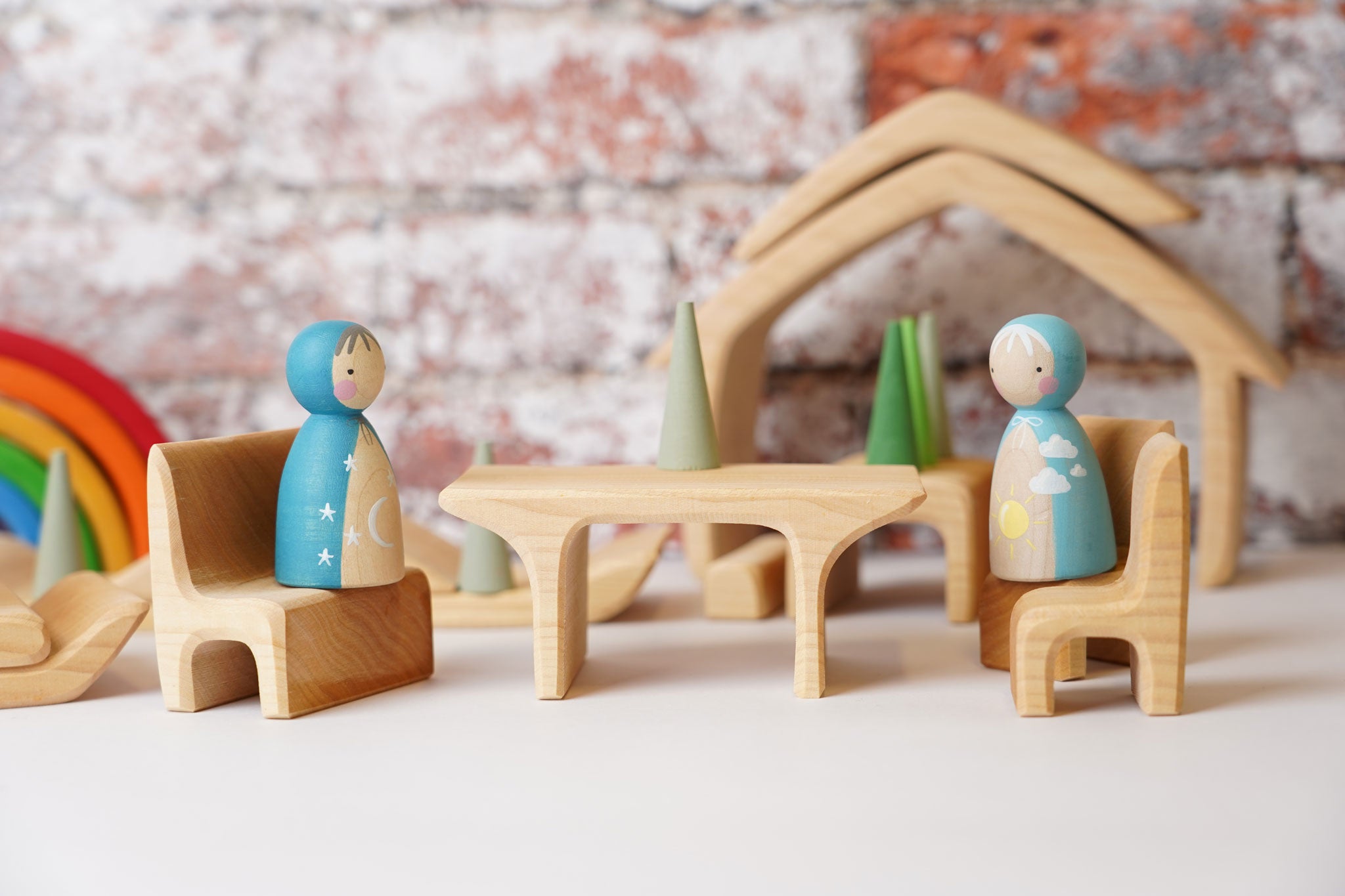 Two wooden peg dolls placed on teh seat pieces from the Gluckskafer Natural All-In House wooden toy. The other pieces from the set can be seen in the background. 