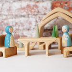 Two wooden peg dolls placed on teh seat pieces from the Gluckskafer Natural All-In House wooden toy. The other pieces from the set can be seen in the background. 