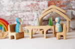 Two wooden peg dolls placed on teh seat pieces from the Gluckskafer Natural All-In House wooden toy. The other pieces from the set can be seen in the background. 