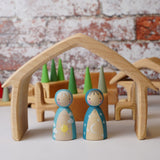 Two wooden peg dolls placed underneath the outer house shaped piece from the Gluckskafer Natural All-In House wooden toy.