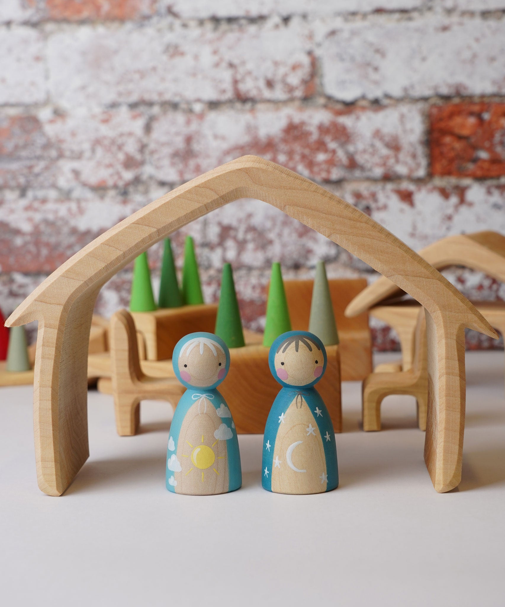 Two wooden peg dolls placed underneath the outer house shaped piece from the Gluckskafer Natural All-In House wooden toy.