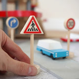 Adult hand holding the Gluckskafer miniature zebra crossing traffic sign next o a play road set