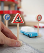 Adult hand holding the Gluckskafer miniature zebra crossing traffic sign next o a play road set