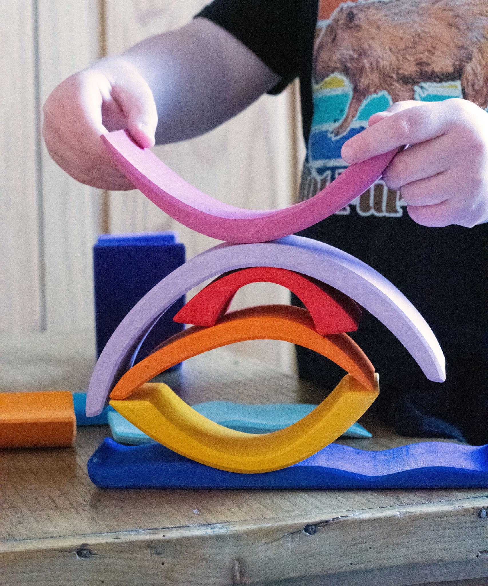 A child creating a stack using pieces from the Glückskäfer wooden Purple Sunset Set Toy.
