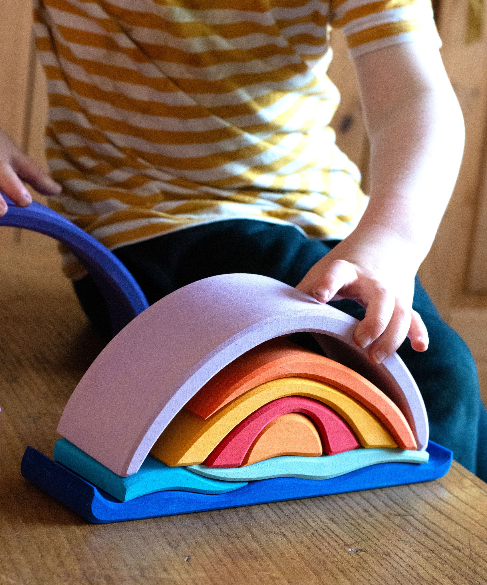Glückskäfer wooden Purple Sunset Set Toy. A child's hand can be seen placing pieces on the stack. 