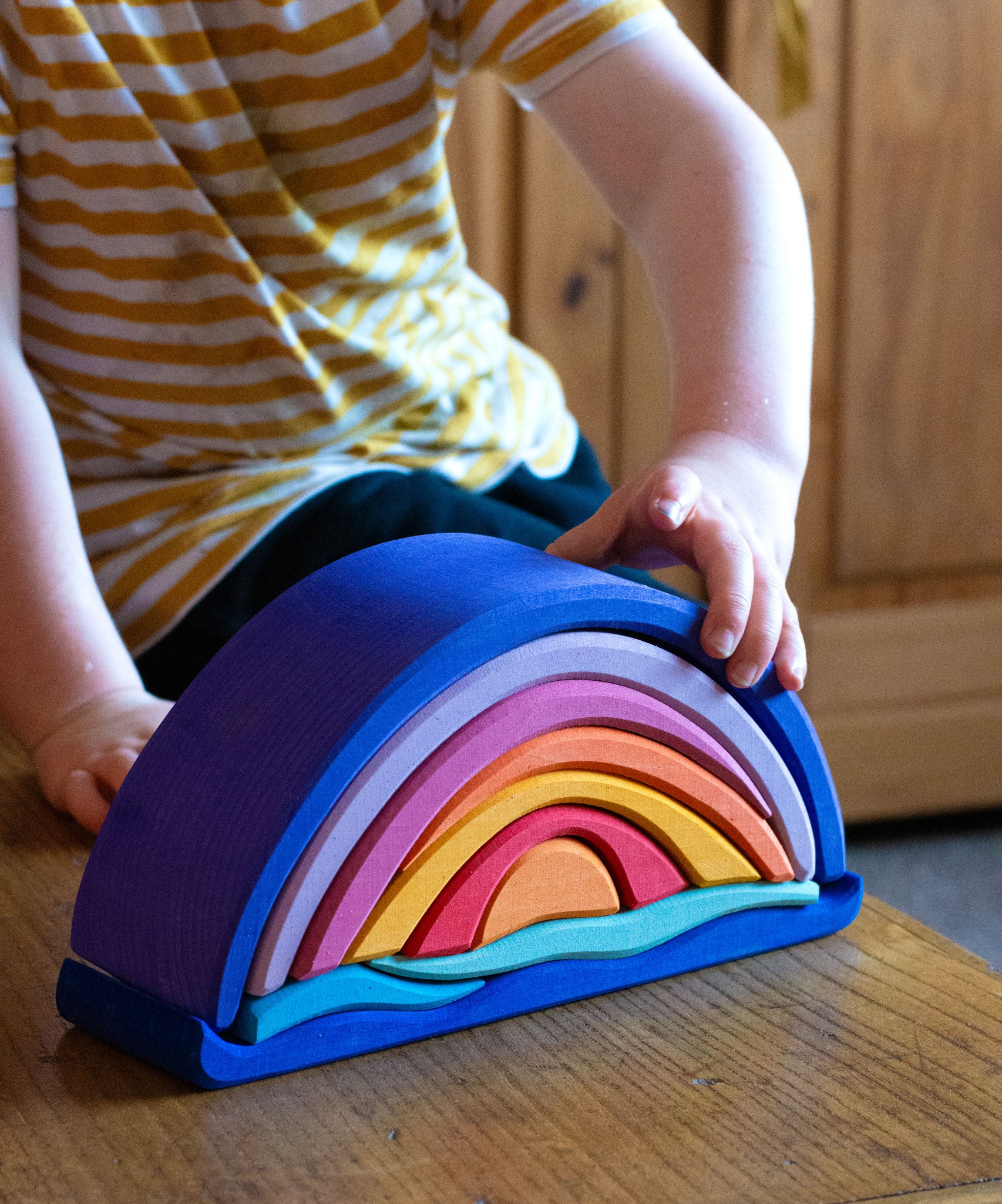 Glückskäfer wooden Purple Sunset Set Toy. A child's hand can be seen placing pieces on the stack. 