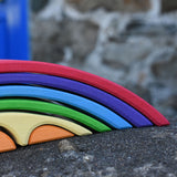 A close up of the front of the Gluckskafer Rainbow Bridge wooden toy. The bridge has been placed on a stone wall outdoors. 