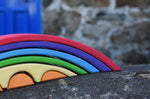 A close up of the front of the Gluckskafer Rainbow Bridge wooden toy. The bridge has been placed on a stone wall outdoors. 