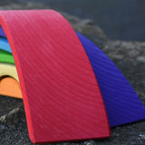 A close up of the largest red bridge piece from the Gluckskafer Rainbow Bridge wooden toy. The natural wood grains are showing through the natural dyes, each piece is unique. 
