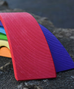 A close up of the largest red bridge piece from the Gluckskafer Rainbow Bridge wooden toy. The natural wood grains are showing through the natural dyes, each piece is unique. 
