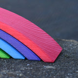 A close up of the largest red bridge piece from the Gluckskafer Rainbow Bridge wooden toy. The natural wood grains are showing through the natural dyes, each piece is unique. 
