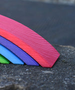 A close up of the largest red bridge piece from the Gluckskafer Rainbow Bridge wooden toy. The natural wood grains are showing through the natural dyes, each piece is unique. 
