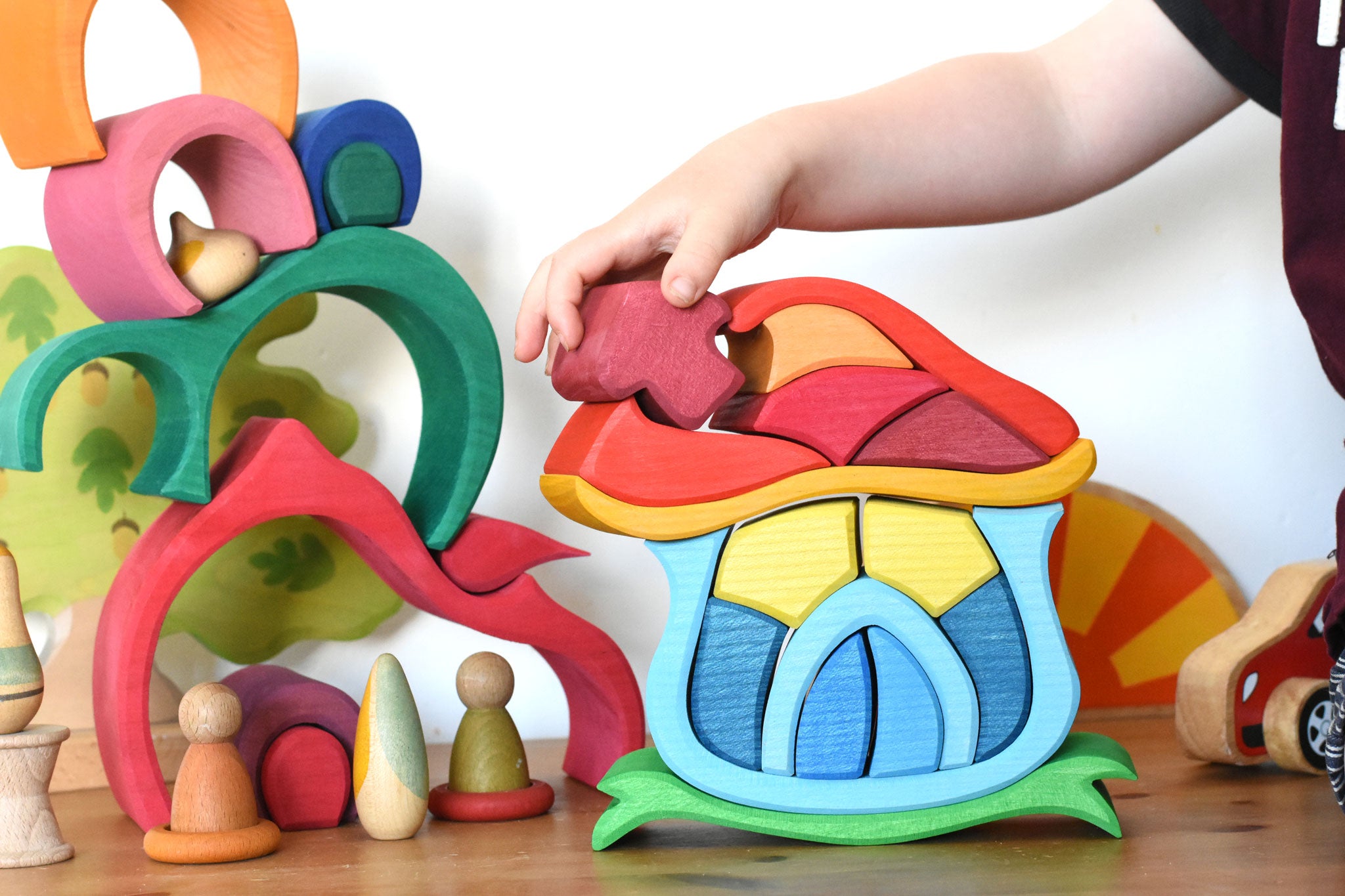 A child playing with the Glückskäfer Mushroom House wooden stacking toy. The are placing the mushroom shaped wooden block back into place. 