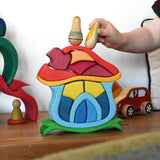 A child playing with the Glückskäfer Mushroom House wooden stacking toy. They are placing Grapat wooden toy figures on the roof. 