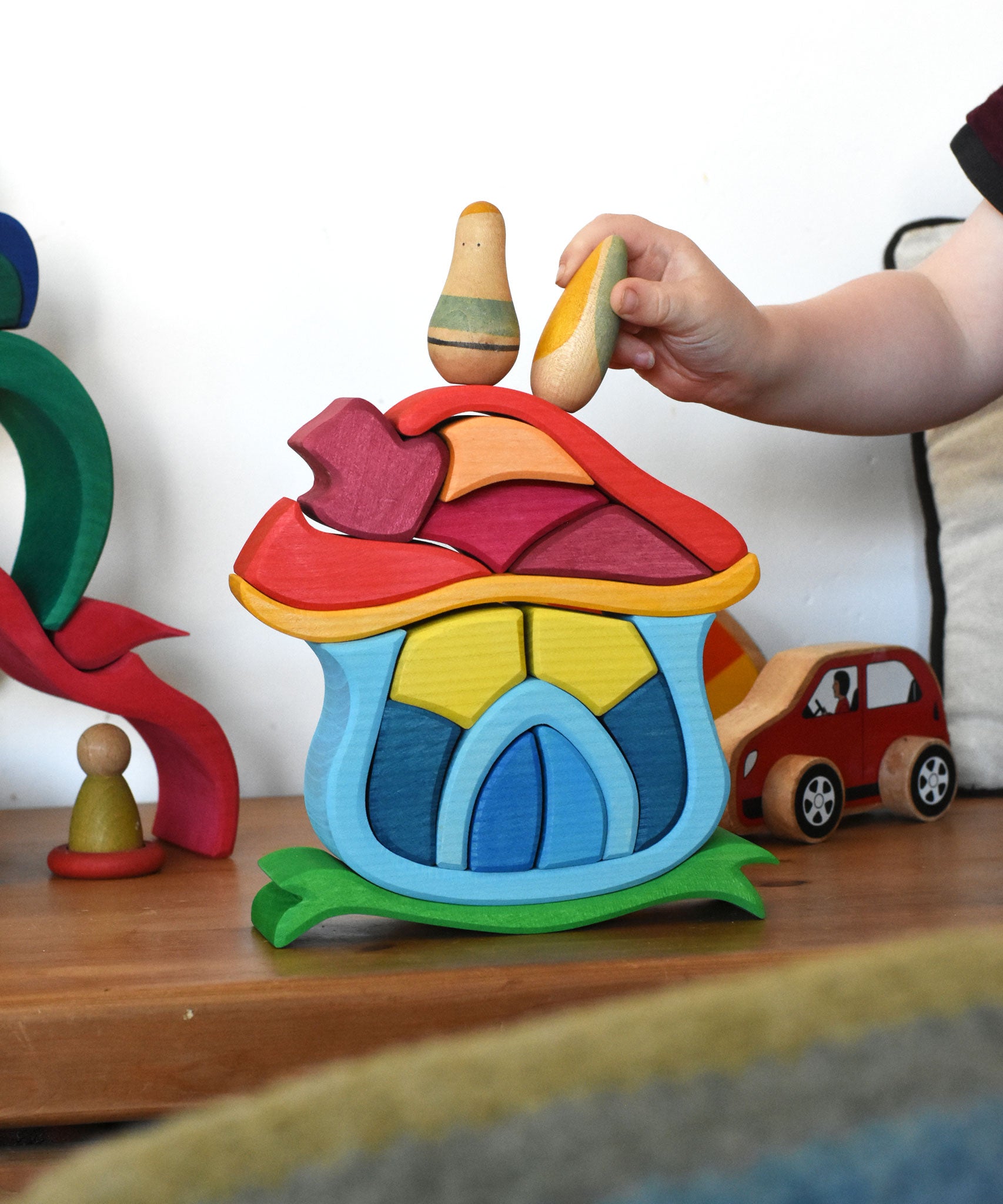 A child playing with the Glückskäfer Mushroom House wooden stacking toy. They are placing Grapat wooden toy figures on the roof. 