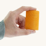 A close up of the small orange block from the Gluckskafer rainbow bridge stacker held by an adult hand showing the scale of the block