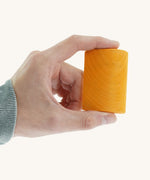 A close up of the small orange block from the Gluckskafer rainbow bridge stacker held by an adult hand showing the scale of the block
