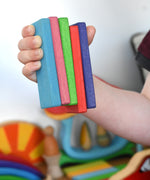 A close up of 5 wooden slats from the Glückskäfer 60 Tower Building Slats Set in a child's hand. 
