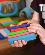 A close up of 5 wooden slats from the Glückskäfer 60 Tower Building Slats  Set in a child's hands.