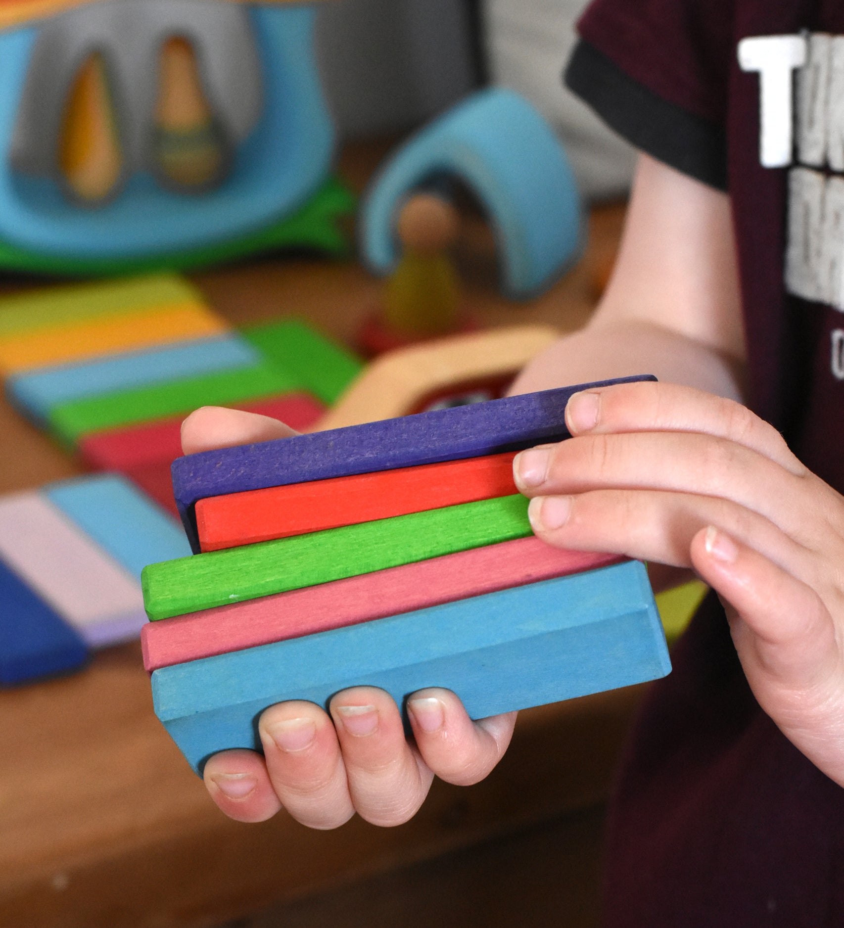 A close up of 5 wooden slats from the Glückskäfer 60 Tower Building Slats  Set in a child's hands.