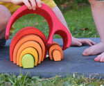 A close up of a child's hands playing with the Glückskäfer Red 8 Piece Arch House.